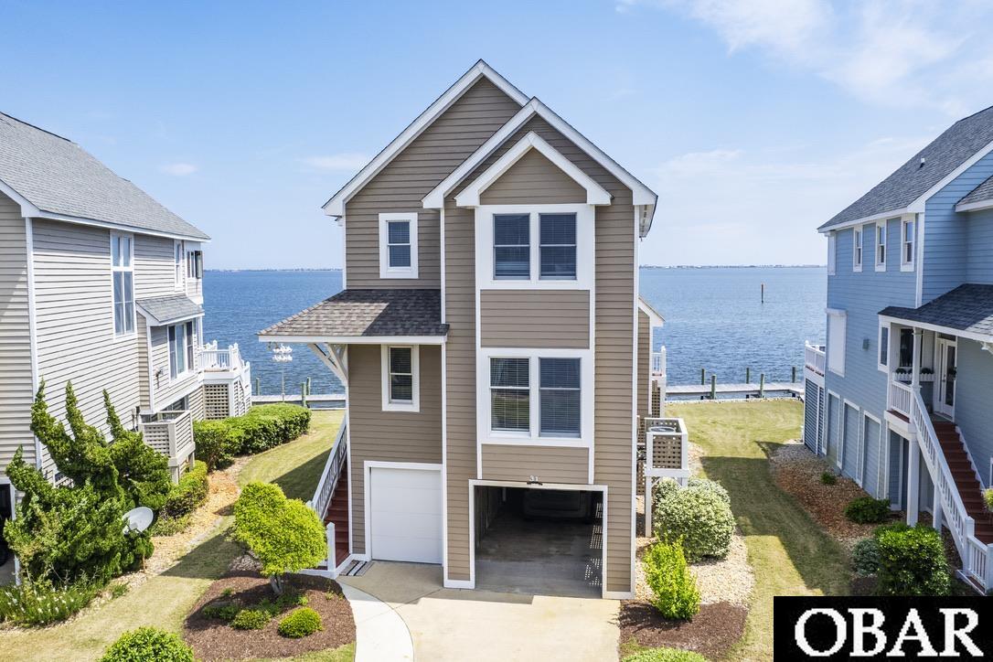 Located on the soundfront, close to great fishing, boating and of course our world famous Outer Banks beaches, this 4 bedroom 3 bathroom home in the Pirate's Cove community is turn-key AND comes with it's own boat slip assignment. The sweeping sound views greet you as you walk thru the door into the open concept living and dining space. Enjoy waterfront dining in your own home. The kitchen features granite countertops, stainless steel appliances, farmhouse sink and pantry. Cozy up to the gas fireplace in the fall and winter, and enjoy the water views all year. A porch spans the entire east facing side of this level, with a sunken hot tub on one side. It's a great spot to relax after a long fun day on the beach or on the water. Enjoy the shade under the covered portion of the porch, or step out into the sunshine, it's your choice, you have both options! This level of the home also features a bedroom with en suite bathroom and laundry space. Walk up the stairs to another large bedroom with its own private soundfront covered porch, en suite bathroom and fantastic water views. There are two other bedrooms on this level, as well as a jack and jill bathroom. Every room comes fully furnished and decorated in a coastal and fishing inspired theme. The ground level features a large conditioned storage space. Some owners opt to park a golf cart in this space, and still have plenty of room for beach toys and fishing gear. An outdoor shower and stainless steel fish cleaning table with sink round out the ground level in this waterman/waterwomans ideal property. AND this home comes with it's own 25' boat slip assignment. It's steps away, on the canal side, keeping your vessel more protected from the wind. The Pirate's Cove community is centrally located between Nags Head and the town of Manteo, in very close proximity to the Oregon Inlet Marina and fishing center and features a marina, restaurant, tiki bar, multiple pools, fitness center, tennis and playground. It's a popular choice for boaters and fishing enthusiasts and hosts multiple fishing tournaments and events throughout the year, that bring owners and guests together to enjoy the fruits of our waters. Beachgoers love the ease of access to the ocean, while living in a well maintained community with amenities. This section of Pirate's Cove includes landscaping, so you dont have to do anything, just enjoy the Outer Banks. Come tour this fantastic waterfront home and enjoy all the Outer Banks has to offer. Use it for yourself or as a rental income producing investment or both! New roof, carpet and paint inside and outside in 2022.