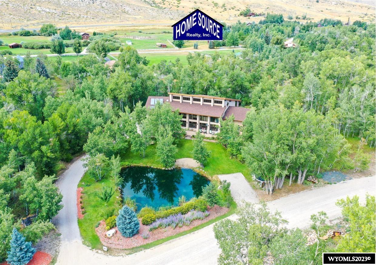 This riverfront, custom home is located in the foothills of the Wind River Mountains of Wyoming. It’s like living in the mountains on a forested 2.54 acre lot with an abundance of streams and trees, river and mountain views, yet only 7 minutes from the darling Main Street of the City of Lander.  House Features: This custom 6,522 sq ft home includes 4 bedrooms and 4.5 bathrooms, all master suites with private bathrooms, and three of the bedrooms have private balcony access. There is a lovely main-level master bedroom, with an adjacent laundry room. The mother-in-law suite has its own kitchenette, bathroom, laundry service and separate access, providing a great opportunity for multi-generational housing or Airbnb interest. The entry sunroom, atrium, 31 foot vaulted ceilings and the grand, open living spaces are illuminated with floor-to-ceiling south-facing windows, providing an exceptional view from every room with a welcoming and bright feel. The heating includes areas of in-floor heat, built-in wall heaters, a wood burning stove and a passive solar design. The home is very well insulated, with R-50 wall and R-60 roof construction, making the home efficient and comfortable with very little effort year round. There is a craft-room that could easily serve as a 5th bedroom, plus an office and a second family room. The main-level living room, dining and kitchen with breakfast bar is open and ideal for large gatherings. Some noteworthy construction features include: Hand finished alder wood doors, quality wood casement windows, zebrawood kitchen island, hickory cabinetry in the kitchen, cork flooring in the kitchen, Brazilian hardwood bamboo flooring throughout the home, attractive exposed beams, wrought iron/wood railings, tasteful Mission Style fixtures, on-demand hot water, foam insulated and spacious crawlspace, low-maintenance stucco exterior and 50-year rated architectural shingles. Land/Site and Outbuilding Features: The location is a rare-find, tucked within 10 minutes between the City of Lander and Sinks Canyon State Park. There are two private wells; one with a solar pump to fill the wetland pond, the other to bring excellent drinking water into the home. The attached 31’x30’ attached garage is heated and has access to both the mother-in-law quarters and main-house. On the backside of the house there are 2 full hook-ups for RVs (both 30 & 50 amp service). The property has river frontage, and it borders a nice green belt area where the Popo Agie River flows. The outdoor amenities include a wraparound covered balcony deck, large open patio, firepit area and multiple spots throughout the land to sit and relax. The mature, manicured lawn is on an automatic sprinkler system.  This exquisite home on its prime lot is a rare opportunity to own the jewel of the Wind River Valley.